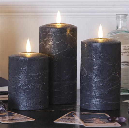 Three dark marbleized candles on a surface with cards and decorative items.