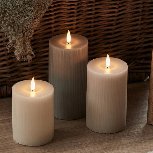 Three lit candles of different sizes on a wooden surface with a woven basket in the background.