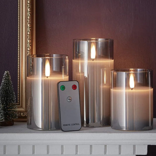 Set of three candle-like lights with a remote control on a surface against a dark wall.